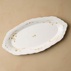 a white and gold serving platter on a tan surface with an olive branch design