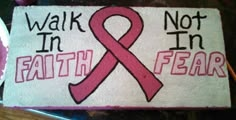 a hand painted sign with a pink ribbon on it that says walk in faith not in fear