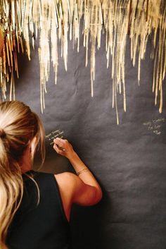 a woman writing on a blackboard with straws hanging from the ceiling and text that reads 40 ways to stay golden on your wedding day