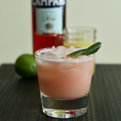 a pink drink in a glass with a green garnish on the rim next to a bottle