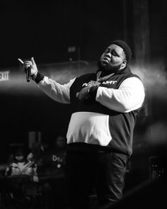 a man standing on top of a stage with his hand up in the air while wearing a vest