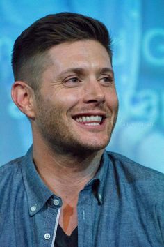 a close up of a person wearing a blue shirt and smiling at the camera with a smile on his face