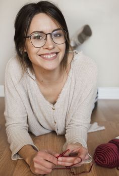 a woman laying on the floor with her hands together and knitting yarn in front of her