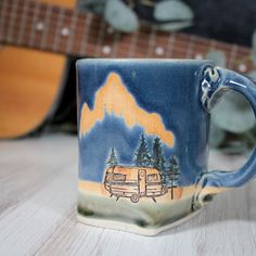 a coffee cup with a camper on it sitting next to a guitar and tree