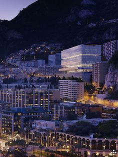 an aerial view of a city at night with mountains in the background and lights on