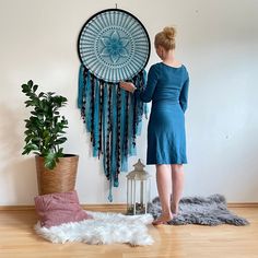 a woman standing in front of a wall hanging with a blue dream catcher on it