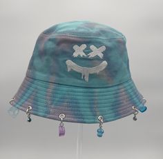 The Smiley Face Bucket Hat is the perfect addition to any festival or rave outfit. Made to be both stylish and functional, this bucket hat is a must-have clothes accessory for any fashion-forward individual.  Key Features: - Stylish design with 12 charms.  - Versatile enough for both festivals and raves. - Provides ample sun protection on bright days. Crafted with high-quality materials, this bucket hat guarantees long-lasting use while keeping your head cool and comfortable. Its sleek design al Fun Adjustable Hats For Streetwear, Adjustable Fun Hat For Streetwear, Fun Adjustable Streetwear Hats, Adjustable Hats For Summer Streetwear, Adjustable Summer Hats For Streetwear, Adjustable Summer Streetwear Hats, Blue Bucket Hat With Curved Brim For Festivals, Blue Bucket Hat With Short Brim For Festivals, Summer Festival Snapback Hat