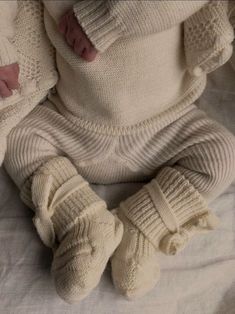 a baby laying on top of a bed wearing white knits and socks with their feet up