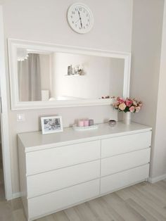 there is a white dresser with flowers on it and a clock above the top shelf