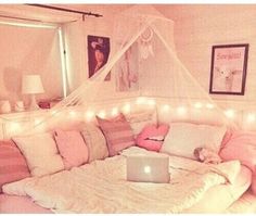 a laptop computer sitting on top of a bed covered in blankets and pillows with fairy lights