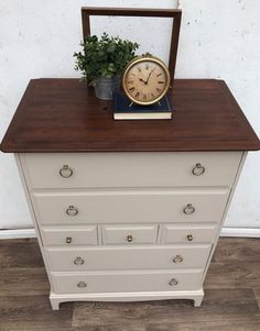 a clock sitting on top of a white dresser next to a potted plant in a vase