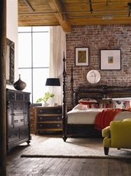 a bedroom with brick walls and wooden flooring has a bed, chair, dresser and window