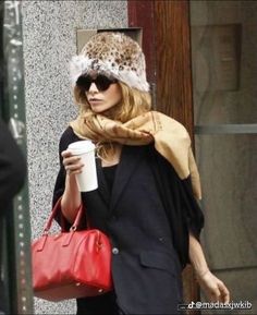 a woman walking down the street carrying a red purse and a coffee in her hand