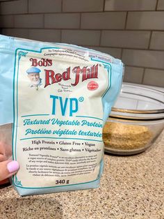 a hand holding a bag of red mill tvp on top of a kitchen counter