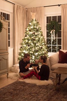 a man and woman sitting in front of a christmas tree