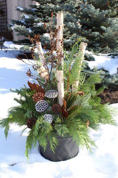 a planter filled with pine cones and other plants in the middle of snow covered ground