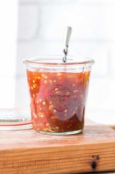 a jar filled with food sitting on top of a wooden cutting board next to a spoon