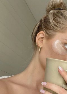 a woman is holding a cup and looking at her face with clear patches on her cheek