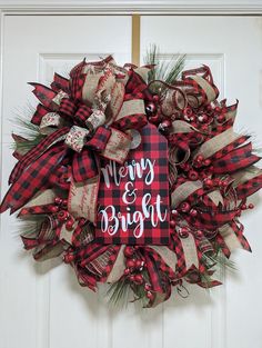 a red and black christmas wreath with merry and bright written on the front, hanging on a white door