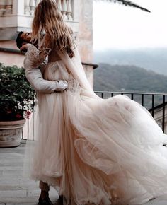 a woman in a wedding dress holding onto another woman's back as they stand on a balcony