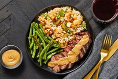 a plate with meat, rice and asparagus next to a cup of sauce