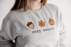 Get ready for fall in our cute 'cozy season' pullover sweatshirt. Long Sleeve T-shirt With Embroidered Graphics For Fall, Cozy Embroidered Sweatshirt For Winter, Winter Embroidered Sweater For Loungewear, Winter Loungewear Tops With Embroidered Graphics, Winter Embroidered Tops For Loungewear, Cute Cozy Fit Tops For Fall, Casual Embroidered Fall T-shirt, Casual Embroidered T-shirt For Fall, Embroidered Long Sleeve T-shirt For Fall