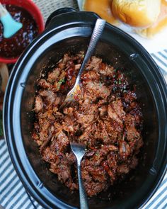 a crock pot filled with pulled pork and bbq sauce next to buns