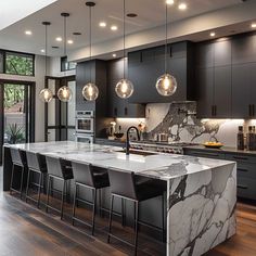 a large kitchen with marble counter tops and black cabinets, along with modern lighting fixtures