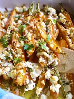 a wooden spoon is in a dish with carrots and feta cheese on it