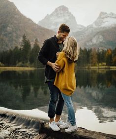 a man and woman standing next to each other on top of a log near water