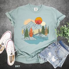 🌄 Embrace the wilderness with our stunning "Mountain Sunrise" tee, exclusively on a high-quality Comfort Colors T-shirt! 🌲 👕 **Product Details - **Design A captivating landscape featuring majestic mountains under a warm, rising sun, complemented by a serene lake and lush, colorful trees. This artwork is a true nature lover's dream, perfectly blending bold and soothing colors for a timeless look. - **Material Crafted with the soft and durable fabric of Comfort Colors®, ensuring both comfort an Outdoor Cotton Printed Tops, Printed Cotton Tops For Outdoor, Spring Graphic Print Tops For Outdoor, Green Summer Adventure Top, Outdoor Cotton Shirt With Sublimation Print, Green Graphic Tee For Hiking, Summer Graphic Print Shirt For Hiking, Summer Graphic Print Shirt For Outdoor, Nature-inspired Graphic Print Crew Neck Top