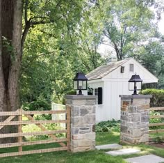 a white shed with two lamps on top of it next to a fence and trees