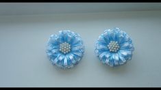 two blue flowers with pearls in the center on a white surface next to each other