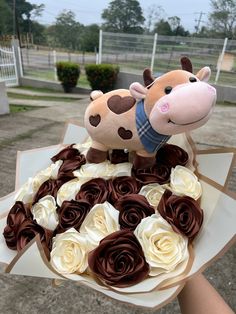 a person holding a cake with two stuffed animals on it's top and roses in the middle