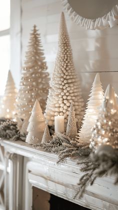 a fireplace mantel decorated with white christmas trees and candles on top of the mantle