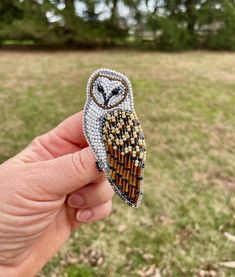 an owl brooch is being held in the air with grass and trees in the background