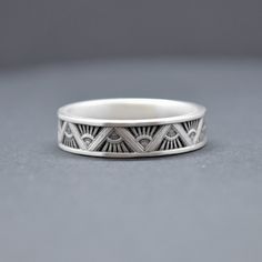 a silver ring with an eye design on the front and sides, sitting on a gray surface