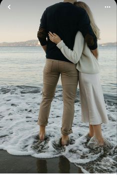 a man and woman standing on the beach with their arms around each other's back