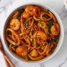 a bowl filled with shrimp and noodles on top of a white table next to chopsticks