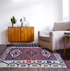 a living room with a rug, chair and potted plant