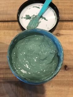 a blue bowl filled with green cream next to a container of yogurt on top of a wooden table