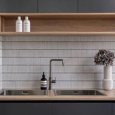 a kitchen with gray cabinets and white tile backsplash, two vases on the counter