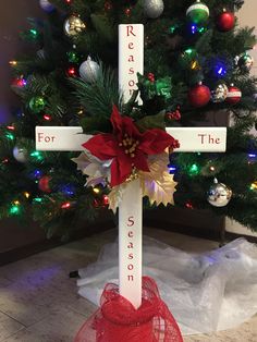 a cross decorated with red and gold ribbon sits in front of a christmas tree that reads ready for the season