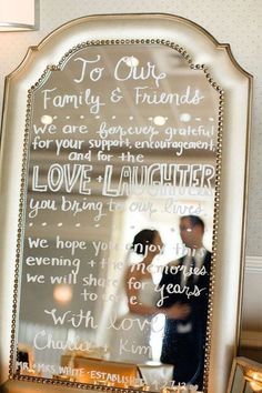 a mirror with words written on it in front of a man and woman standing next to each other