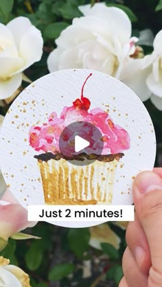 someone holding up a cupcake with pink frosting and a cherry on top that says just 2 minutes