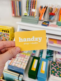 a hand holding up a yellow business card with the words handy shop + studio on it