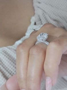 a woman's hand holding a diamond ring in front of her face and the other hand