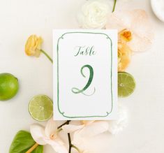 a table number with limes and flowers around it on top of a white surface