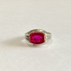 Awesome vintage 10k white gold 1930s era ring featuring a vibrant created ruby! The deep red / pink gem weighs an estimated 3.79 carats, is emerald cut, and securely bezel set. The substantial setting is detailed with decorative designs on the shoulders. Charming vintage piece of fine jewelry for him or her, featuring July's birthstone! ERA - Circa 1930 METAL / MATERIAL - 10k white gold, 1 created ruby (estimated 3.79 carats) [Synthetic ruby contains essentially the same chemical composition &am Classic Red Solitaire Ruby Ring, Vintage Ruby Rings With Polished Finish, Classic Ruby Birthstone Ring, Vintage Red Hallmarked Signet Ring, Classic Red Birthstone Ring With Polished Finish, Classic Ruby Ring With Polished Lab-created Ruby, Classic Pink Ruby Rings, Classic Rings With Polished Finish And Lab-created Ruby, Classic Lab-created Ruby Ring With Polished Finish