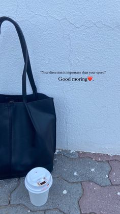 a black purse sitting next to a white wall with a cup of coffee in front of it